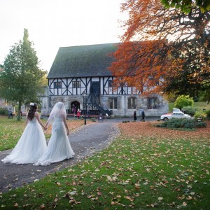 Bride and bridesmaid walk through gardens towards historic building