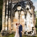 Bride and groom kiss beside abbey ruin